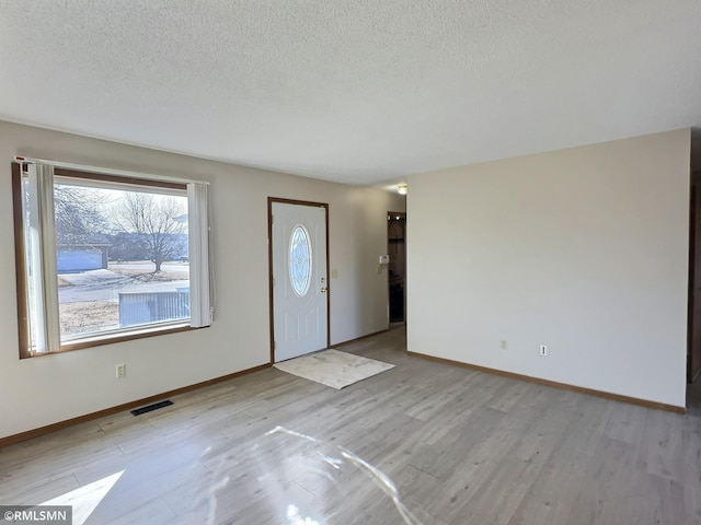 entryway with a textured ceiling, baseboards, visible vents, and light wood-type flooring