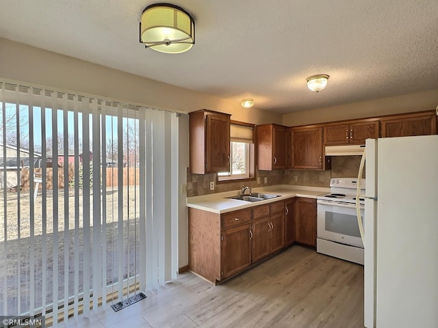 kitchen with white appliances, a sink, light countertops, under cabinet range hood, and backsplash