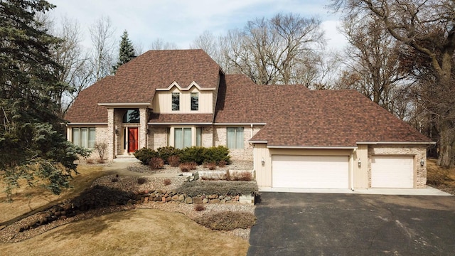 traditional-style house with an attached garage, driveway, and roof with shingles