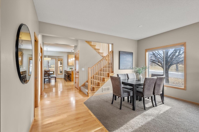 dining space with stairs, baseboards, visible vents, and light wood finished floors