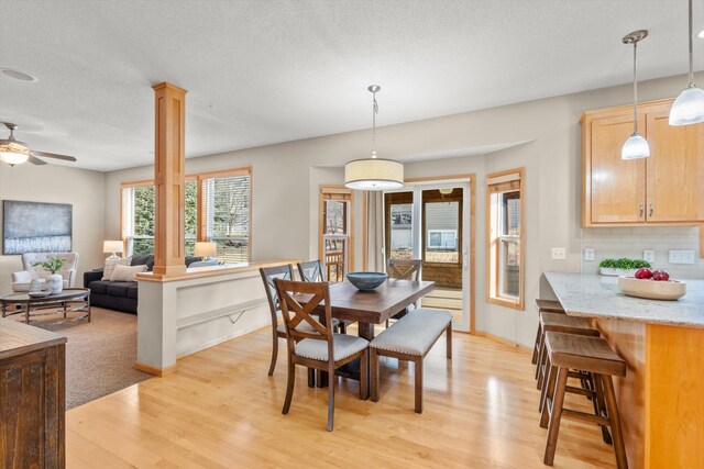 dining space featuring baseboards, decorative columns, light wood-style flooring, a textured ceiling, and a ceiling fan