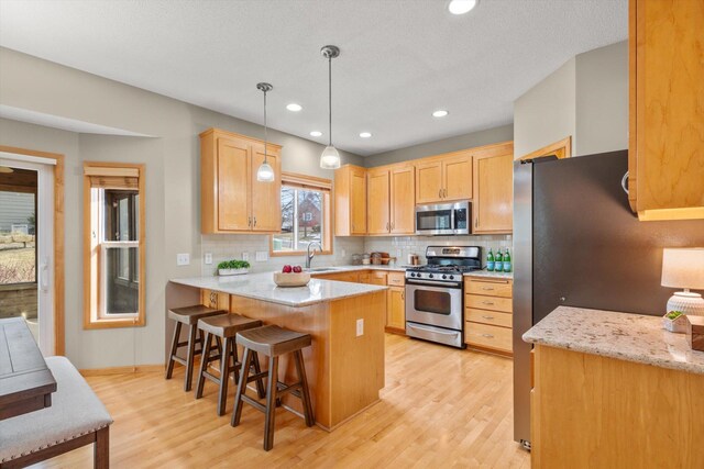 kitchen with tasteful backsplash, light wood-style flooring, appliances with stainless steel finishes, a peninsula, and a sink