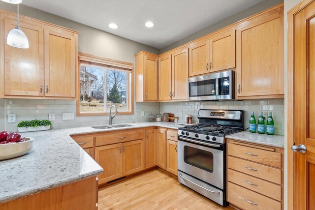 kitchen featuring light stone countertops, a sink, light brown cabinetry, stainless steel appliances, and light wood-type flooring