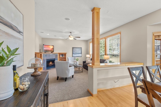 living area with ceiling fan, baseboards, a tiled fireplace, wood finished floors, and ornate columns