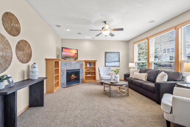 carpeted living area with baseboards, a fireplace, a textured ceiling, and a ceiling fan