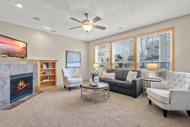 living room with a ceiling fan, a fireplace, carpet floors, and a textured ceiling