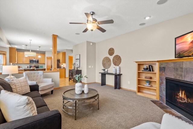 living area featuring light carpet, ceiling fan, a tile fireplace, and baseboards