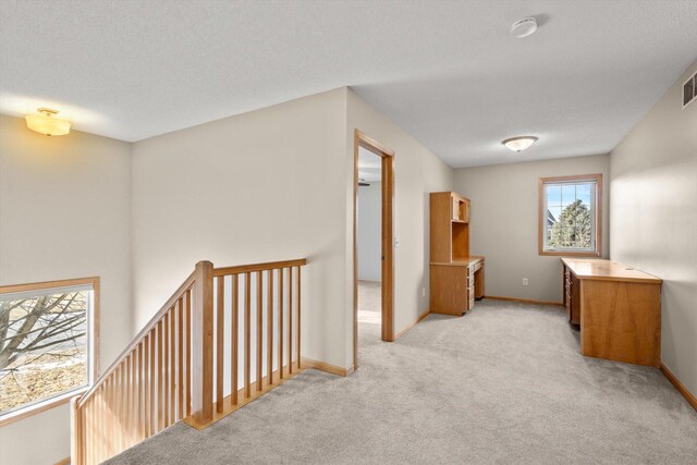 corridor featuring visible vents, baseboards, light colored carpet, and a textured ceiling