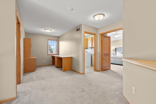 corridor featuring visible vents, baseboards, washer / clothes dryer, a textured ceiling, and light colored carpet