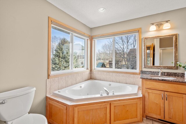 full bathroom with vanity, a jetted tub, toilet, and a textured ceiling