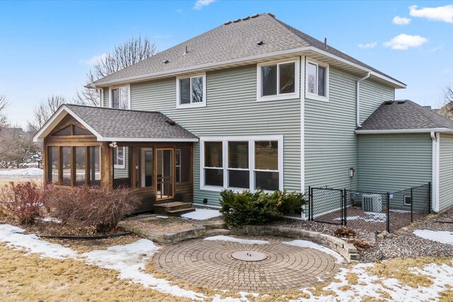 snow covered house with a gate, fence, a sunroom, and roof with shingles