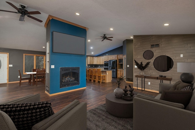 living room with a large fireplace, visible vents, dark wood-style floors, ceiling fan, and wood walls