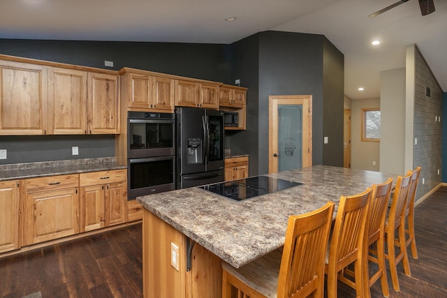 kitchen with dark wood finished floors, a breakfast bar area, lofted ceiling, a kitchen island, and black appliances