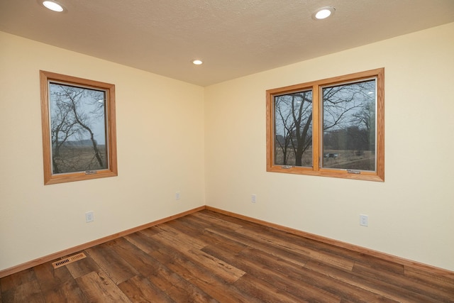 unfurnished room featuring baseboards, visible vents, dark wood-style flooring, a textured ceiling, and recessed lighting