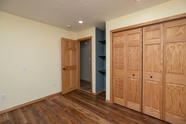 unfurnished bedroom with dark wood-style floors, visible vents, baseboards, and a closet