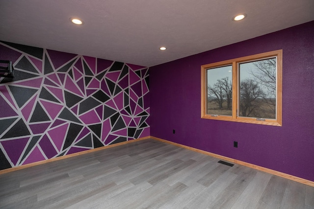 spare room featuring an accent wall, wood finished floors, visible vents, and baseboards