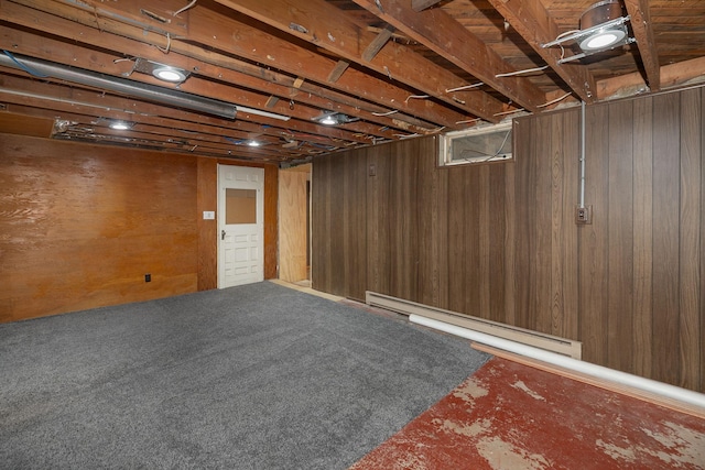 unfinished below grade area featuring a baseboard heating unit, carpet, and wood walls