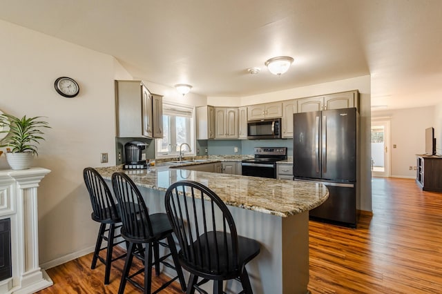 kitchen featuring dark wood-style floors, a peninsula, stainless steel appliances, a kitchen bar, and a sink