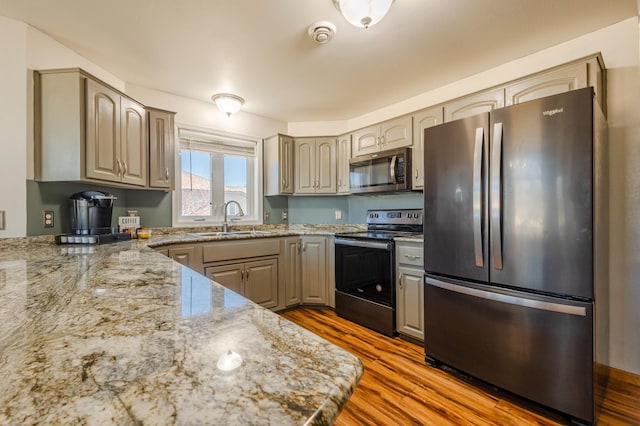 kitchen featuring light stone countertops, appliances with stainless steel finishes, a sink, and wood finished floors