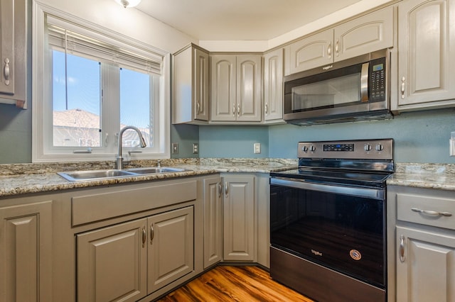 kitchen featuring stainless steel appliances, wood finished floors, a sink, and gray cabinetry