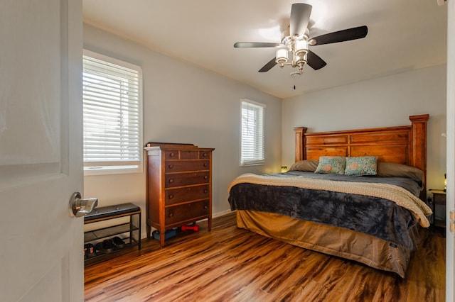 bedroom featuring a ceiling fan, multiple windows, baseboards, and wood finished floors