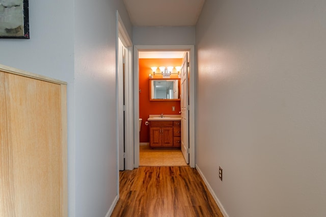 hall featuring a sink, baseboards, and wood finished floors