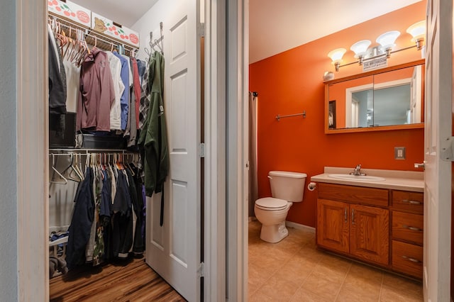 full bath with a walk in closet, baseboards, vanity, and toilet