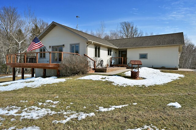 snow covered rear of property featuring a shingled roof, a deck, and a lawn