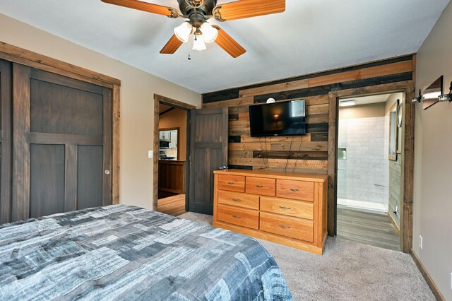 bedroom with a ceiling fan, light carpet, connected bathroom, wooden walls, and baseboards