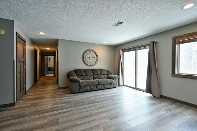 unfurnished living room with a textured ceiling, wood finished floors, visible vents, and recessed lighting