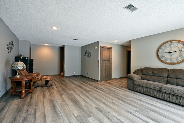 living room with light wood-style floors, visible vents, a textured ceiling, and baseboards