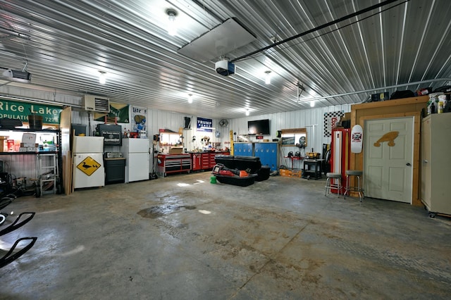 garage featuring a garage door opener, freestanding refrigerator, a workshop area, and metal wall