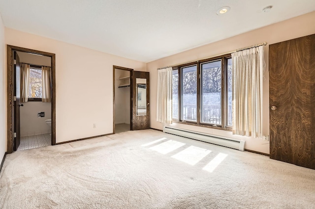 unfurnished bedroom with a walk in closet, light carpet, a baseboard heating unit, connected bathroom, and a closet