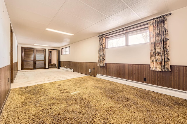 basement with a baseboard heating unit, carpet, wood walls, and wainscoting