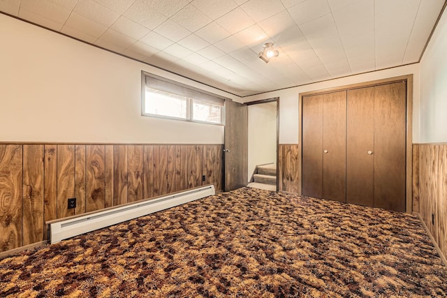 unfurnished bedroom featuring a baseboard heating unit, wooden walls, carpet floors, and wainscoting