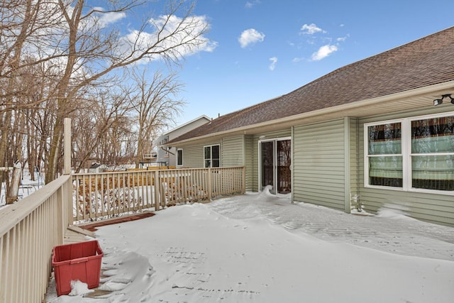 snow covered back of property featuring roof with shingles and a wooden deck