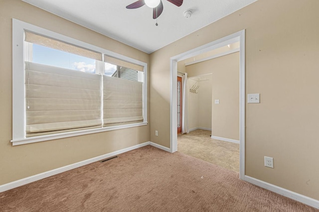 empty room featuring carpet floors, visible vents, baseboards, and a ceiling fan