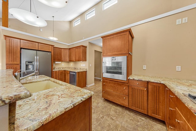 kitchen featuring light stone counters, appliances with stainless steel finishes, brown cabinets, a high ceiling, and a sink