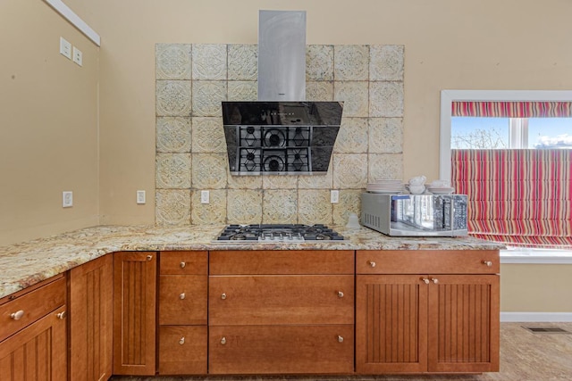 kitchen with brown cabinets, exhaust hood, light stone countertops, and stainless steel gas stovetop