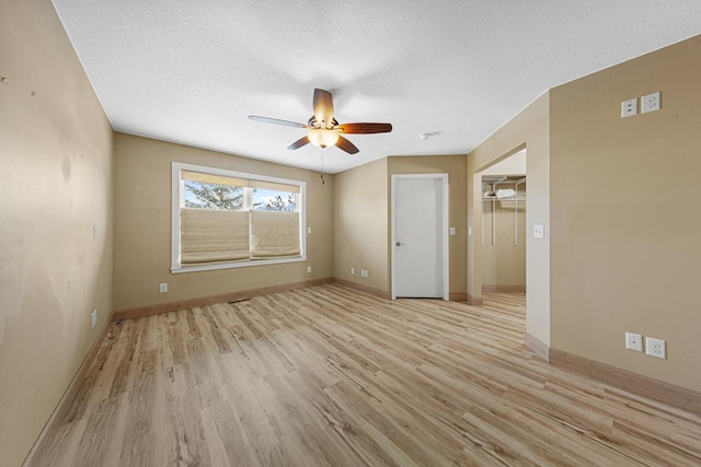 interior space with light wood-style floors, a ceiling fan, baseboards, and a textured ceiling