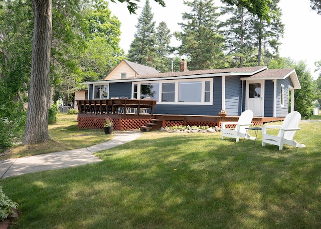 view of front of property featuring a deck, a shingled roof, a chimney, and a front yard