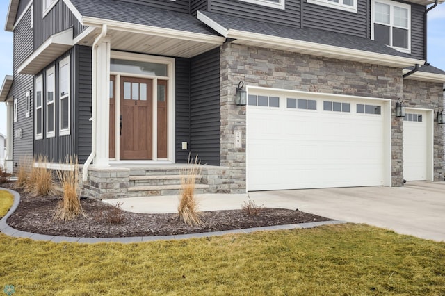 view of exterior entry with a garage, stone siding, roof with shingles, and driveway