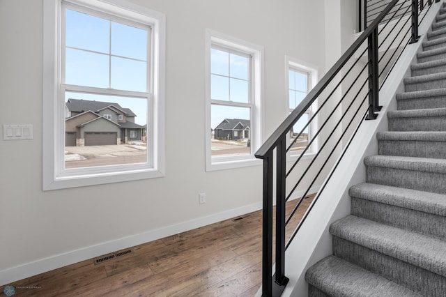 staircase with wood-type flooring, visible vents, and baseboards