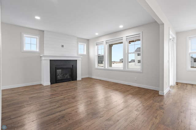 unfurnished living room with a healthy amount of sunlight, hardwood / wood-style flooring, baseboards, and a large fireplace