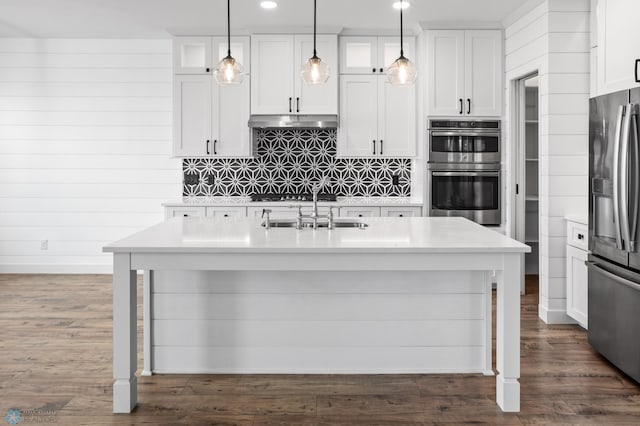 kitchen with stainless steel appliances, decorative backsplash, white cabinets, a sink, and under cabinet range hood