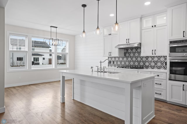 kitchen featuring dark wood-style flooring, stainless steel appliances, light countertops, decorative backsplash, and a sink