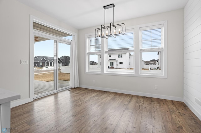 unfurnished dining area featuring baseboards, hardwood / wood-style floors, and a notable chandelier