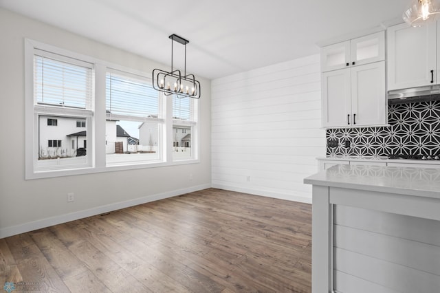 unfurnished dining area with a notable chandelier, wood finished floors, and baseboards