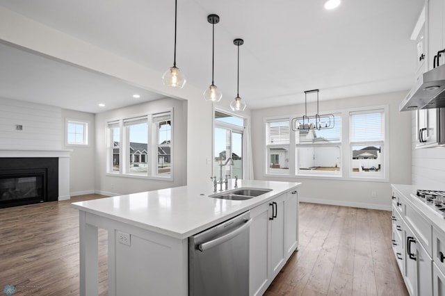 kitchen featuring light countertops, appliances with stainless steel finishes, a kitchen island with sink, a sink, and wood finished floors