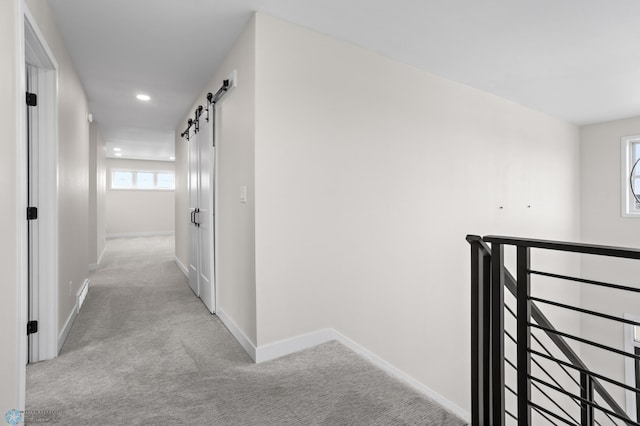 hallway with a barn door, carpet flooring, an upstairs landing, and baseboards